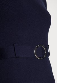 Navyblaues Strickoberteil mit einem breiten Bund und einem runden metallischen Ringdetail in der Taille. Weicher Stoff mit geripptem Material.