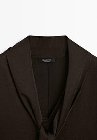 Vêtement marron foncé avec un large col châle et un détail de nœud en tissu à l'encolure, étiqueté Massimo Dutti, fabriqué au Maroc.