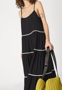 Robe noire sans manches avec un bord en scallop blanc, un design en étages et un tissu fluide ; accompagnée d'un sac plissé vert.