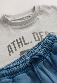 Gray cotton T-shirt with ribbed neckline and dark print text, paired with blue cotton shorts featuring elastic waist and drawstring detail.