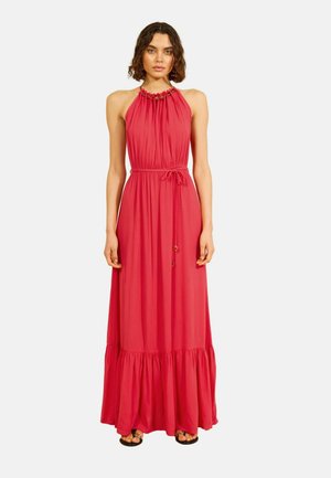 Frau trägt ein ärmelloses rotes Maxikleid mit Neckholder, gebundenem Taillenband und gerafftem Saum, vor einem weißen Hintergrund stehend.