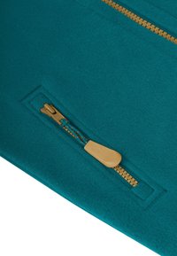 Türkisfarbener Stoff mit einem sichtbaren beigen Reißverschluss. Der Reißverschluss hat einen Ziehgriff und ein dekoratives Muster entlang der Zähne. Glatte Textur.