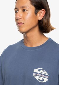 Bawełniana koszulka w kolorze granatowym, z krótkim rękawem i okrągłym dekoltem, z białym i różowym logo na lewej piersi. Gładka tekstura.