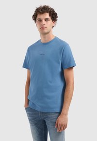 Lichtblauw katoenen t-shirt met korte mouwen en een ronde hals. Voorzien van een kleine zwarte tekstprint met de woorden "PURE PATH" aan de voorkant.