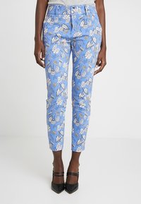 Blue floral patterned pants featuring a tapered fit, two front buttons, and a smooth texture, paired with black pointed heels.