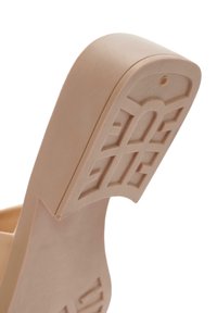 Sandale en caoutchouc beige avec un talon et une semelle texturée et à motifs, ainsi qu'un dos arrondi. Elle semble légère avec une surface lisse et un minimum de détails.