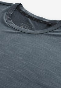 Mörkgrå träningst-shirt med rund krage, som har ett texturerat tyg, diskret mönster och en etikett inuti kragen som anger varumärket.