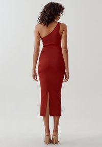 Vestido midi rojo ajustado con diseño de un solo hombro y abertura en la parte posterior. Textura suave. Llevado con tacones nude.