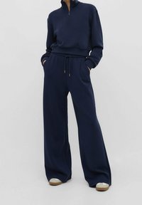 Marineblauwe zip-up sweatshirt met lange mouwen, gecombineerd met brede sweatpants. Zacht materiaal met elastische tailleband en subtiele gouden hardware accenten.