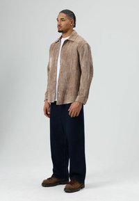 Brown corduroy shirt, white tee underneath, paired with dark baggy pants and brown boots with red laces. Simple, textured design.