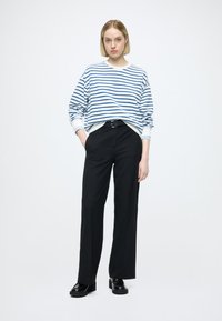 Pull surdimensionné rayé blanc et bleu, pantalon noir taille haute, chaussures plateformes noires épaisses, style minimaliste, fond neutre.