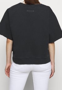 Musta puuvillainen oversized t-paita, jossa on lyhyet hihat, pyöreä kaula-aukko ja hienovarainen valkoinen ommel takahelmassa.