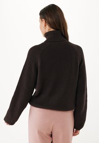 Suéter de canalé marrón oscuro con cuello alto, que presenta un corte relajado y hombros caídos. Combinado con pantalones rosa claro.