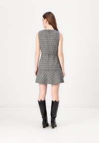 Lyhythihainen tweed-mekko musta-valkoisena, jossa on vartalonmyötäinen vyötärö ja levenevä hame. Yhdistetty polven yli ulottuviin mustiin korkokenkiin.