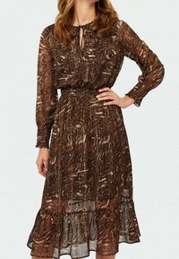 Brun mönstrad klänning med långa ärmar, smockad midja och volangkant. Tillverkad av lätt tyg med ett genomskinligt lager. Detalj med nyckelhål vid halsringningen.