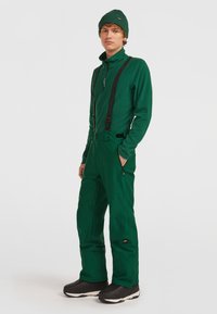 Grön termisk tröja och byxor med justerbara svarta hängslen och fickor. Svarta vattentäta stövlar fulländar outfiten. Slät tygkvalitet.