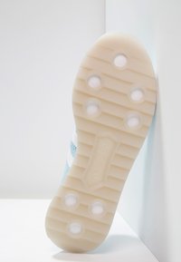 A sneaker sole featuring a light cream color with textured grip patterns and six circular indents, partly visible against a pale background.