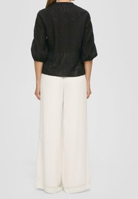 Top de tela negra con un patrón floral texturizado, mangas abullonadas, combinado con pantalones de pierna ancha blancos, mostrando una silueta limpia.
