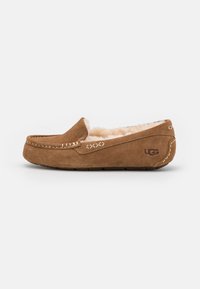 Bruine suede instapslipper met een zachte bontvoering, voorzien van decoratieve stiksels en een rubberen zool, met het label "UGG" aan de zijkant.