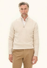Beige ritstrui met een zachte textuur, featuring een hoge kraag, geribbelde mouwen en een ontspannen pasvorm, gecombineerd met tan corduroy broek.
