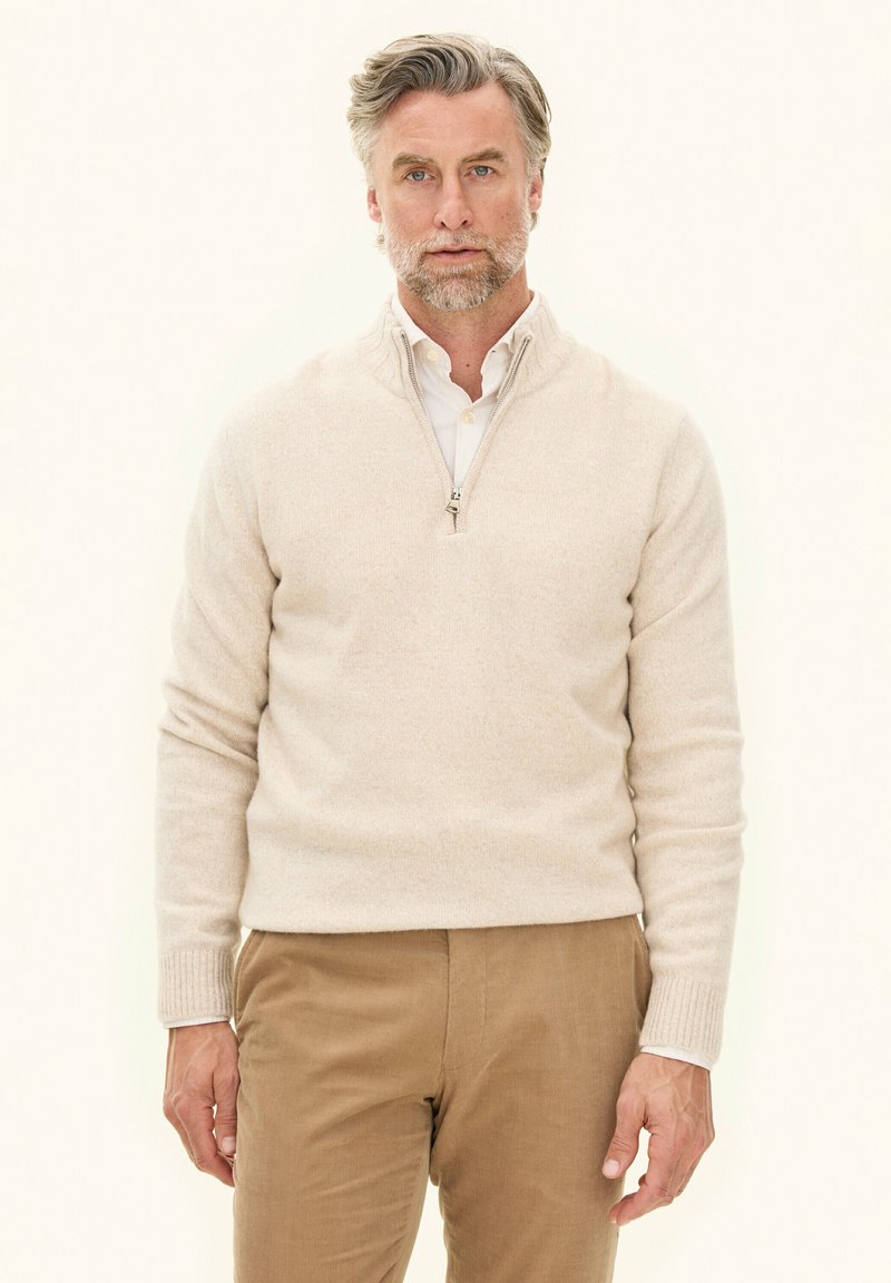 Beige ritstrui met een zachte textuur, featuring een hoge kraag, geribbelde mouwen en een ontspannen pasvorm, gecombineerd met tan corduroy broek.