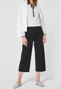 Upravený bílý blazer přes bílou blůzu s černou kravatou, doplněný černými zkrácenými kalhotami. Světle šedé nazouvací boty dotvářejí vzhled.