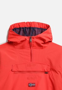 Chaqueta impermeable roja con capucha, que cuenta con un bolsillo frontal con cremallera y un pequeño emblema con una bandera. Textura suave, puños elásticos.