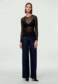 Must aga läbipaistev pikkade varrukatega pluus musta tankiga, kombineerituna laienevate tume denimist teksade ja mustade kontsadega. Siledad ja tekstureeritud materjalid.