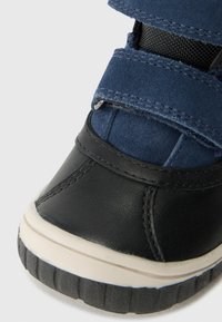Zwarte leren en blauwe suède sneakers met klittenbandsluitingen, een gestructureerd oppervlak, rubberen zool en contrasterende witte rand aan de rand.
