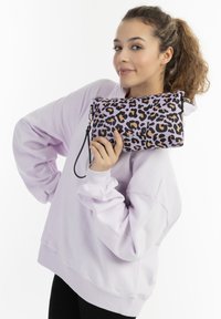 Borsa a tracolla con stampa leopardata in viola, caratterizzata da una superficie liscia, chiusura con zip e cinturino da polso rimovibile. Abbinata a un felpa over-size lavanda.