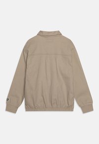 Ljusbeige lätt jacka med krage, elastisk nederkant och ärmslut. Har en sydd etikett på vänster ärm. Materialet verkar slätt.