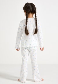 Ensemble de pyjama blanc avec des motifs floraux bleus, comprenant des manches longues et un pantalon évasé. Tissu texturé avec des poignets et un ourlet volants.