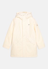 Parka chiara in crema con cappuccio, realizzata in un tessuto liscio. Presenta due tasche frontali, chiusure a pressione e un piccolo logo sulla manica.