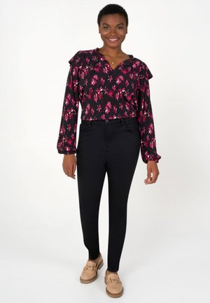 Zwarte bloemenblouse met gerimpelde schouders, gecombineerd met zwarte skinny pantalons en lichtbruine loafers met gouden hardwareaccenten.