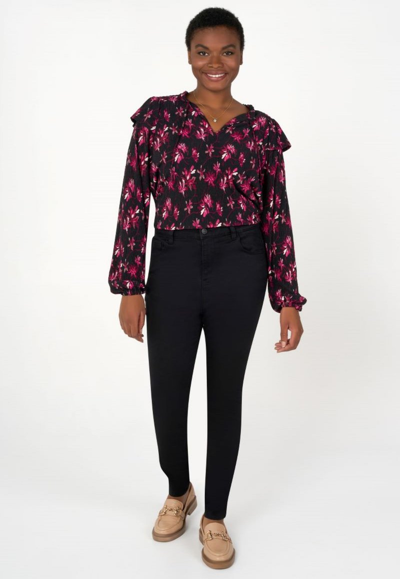 Blouse noire à motifs floraux avec des épaules à volants, associée à un pantalon skinny noir et des mocassins marron clair avec des accents en métal doré.