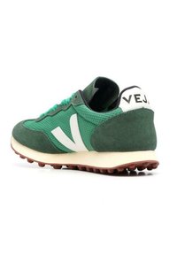 Shoe atlético verde com material em malha e camurça, detalhe de logotipo branco, colarinho almofadado e sola de borracha com sulcos. A vista traseira mostra o logotipo no calcanhar.