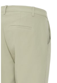 Pantalon beige avec une poche passepoilée à l'arrière, des passants pour ceinture et une poche sur la couture latérale, vu de l'arrière côté droit.