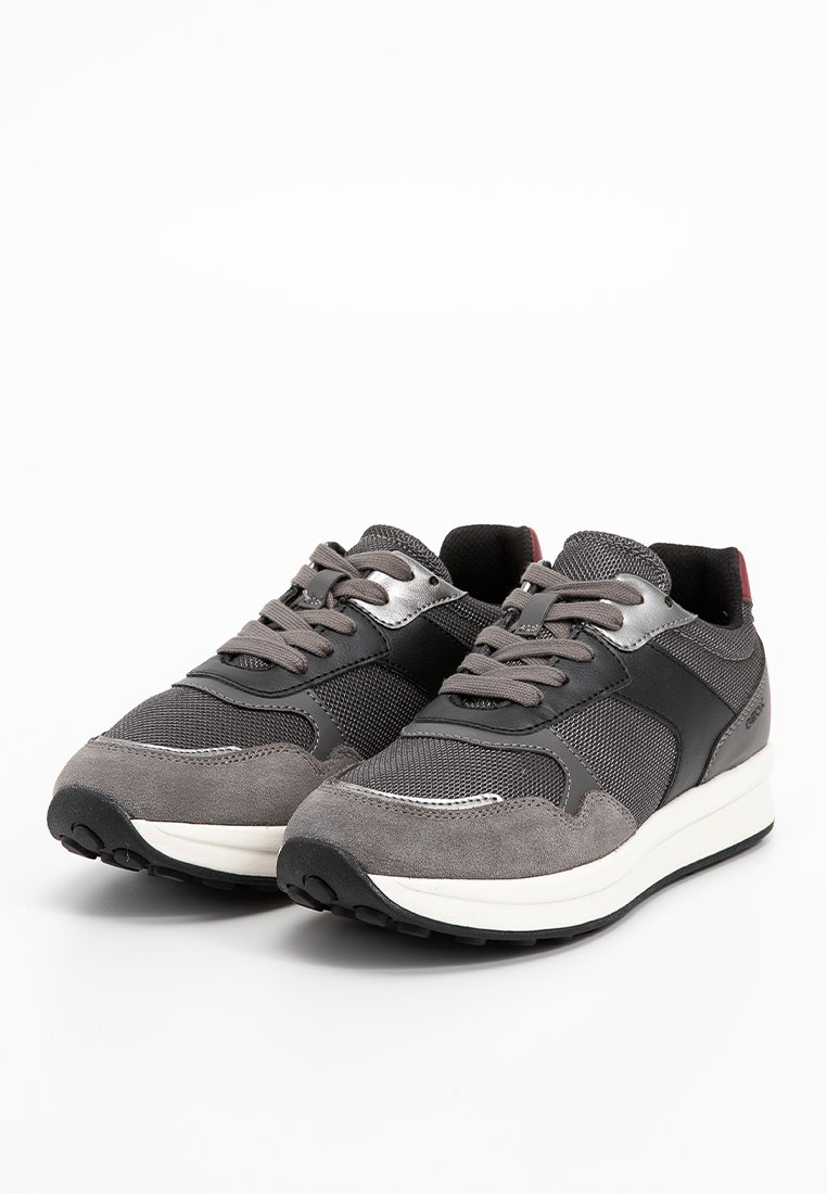 Un paio di sneaker atletiche grigie e nere con pannelli in mesh e suede, lacci legati e suole imbottite bianche su uno sfondo bianco.