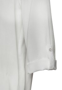 Chemise blanche à boutons, avec des manches retroussées, présentant une texture de tissu douce et une fermeture à un bouton sur chaque poignet. Design épuré et minimal.
