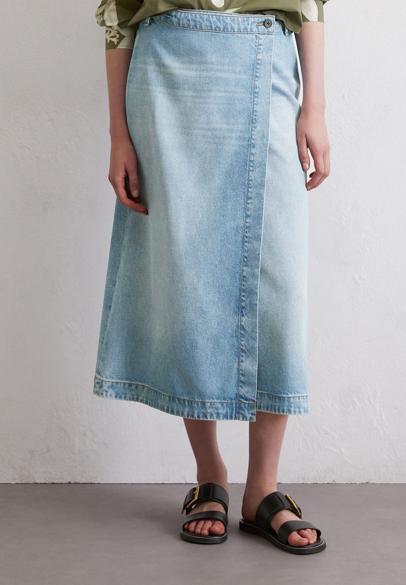 Light blue denim skirt with a high waist, side button closure, and a knee-length hem. Paired with black sandals featuring a gold buckle.