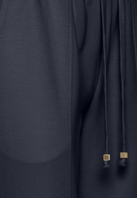 Mörk marinblå joggers i tyg med en slät struktur, elastisk midja och dragkedjor med guldaccenter. Har en minimalistisk design utan ytterligare mönster.