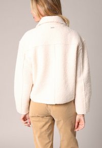 Witte fleece jas met een kraag, verlaagde schouders en details in de achternaad, gecombineerd met beige corduroy broek.