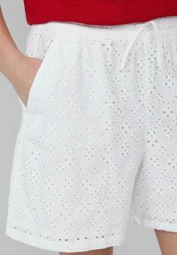 Witte katoenen shorts met een decoratief oogjespatroon, voorzien van een elastische tailleband en twee zijzakken.