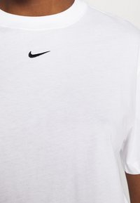 T-shirt bianca in cotone con scollo rotondo, dotata di un piccolo logo Nike ricamato in nero sul petto. Tessuto liscio, maniche corte.