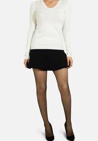 Pull blanc à manches longues et col en V associé à une jupe évasée noire, des collants transparents noirs à pois, et des escarpins noirs.
