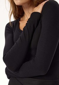 Czarna, długosleeve'owa bluzka o prążkowanej strukturze, z okrągłym dekoltem, charakteryzująca się dopasowanym krojem i gładką fakturą, zaprezentowana na jasnym tle.