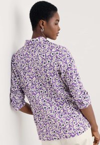 Lila virágmintás ing felgöngyölt ujjakkal, fehér virágokkal és tengerészkék díszítéssel, könnyű anyagból készült.