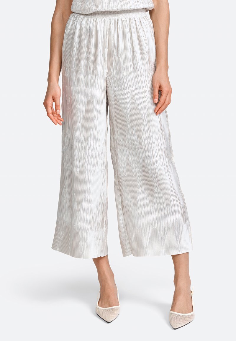 Pantaloni a palazzo a pieghe grigio chiaro con cintura elastica, caratterizzati da una leggera lucentezza e una texture verticale, abbinati a scarpe con tacco alto color crema.