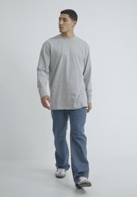 Camisa gris de manga larga con cuello redondo, combinada con jeans azules y zapatillas, con un corte relajado y una textura de algodón suave.
