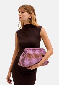 Borsa a tracolla in tessuto simile alla pelliccia nei colori viola e marrone, con una texture morbida, caratterizzata da un design pieghevole. Modello che tiene la borsa indossando un elegante abito scuro.